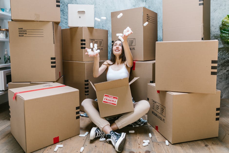 Inside a residential kitchen space during the packing and home relocation process, there are four cardboard boxes labeled 'STUFF', 'CLOTHES', 'BOOKS', and 'PILLOWS' written in marker. The boxes are pl